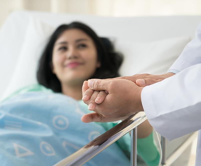 doctor holds hand of patient in hospital bed