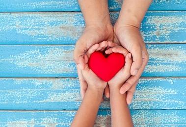 Adult and child hands holding a heart.