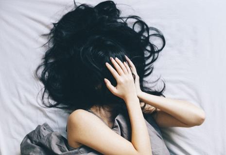 A woman in bed covering up her face with her hair.
