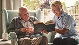 A caregiver reads to a senior man.